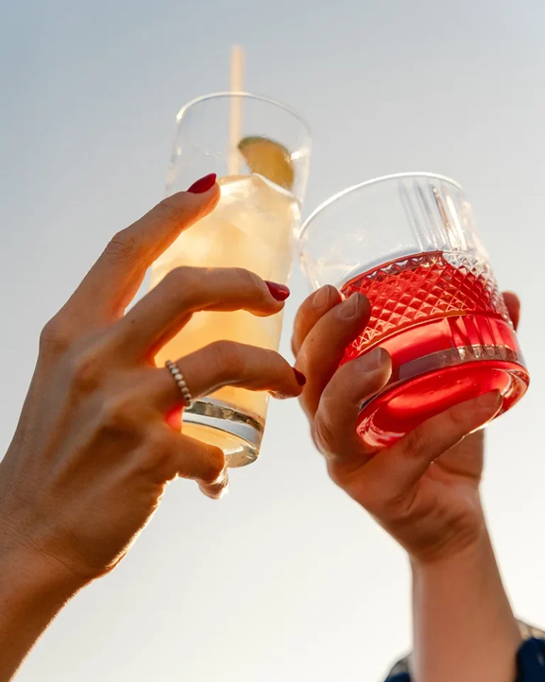 two women clink their cocktails on a rooftop