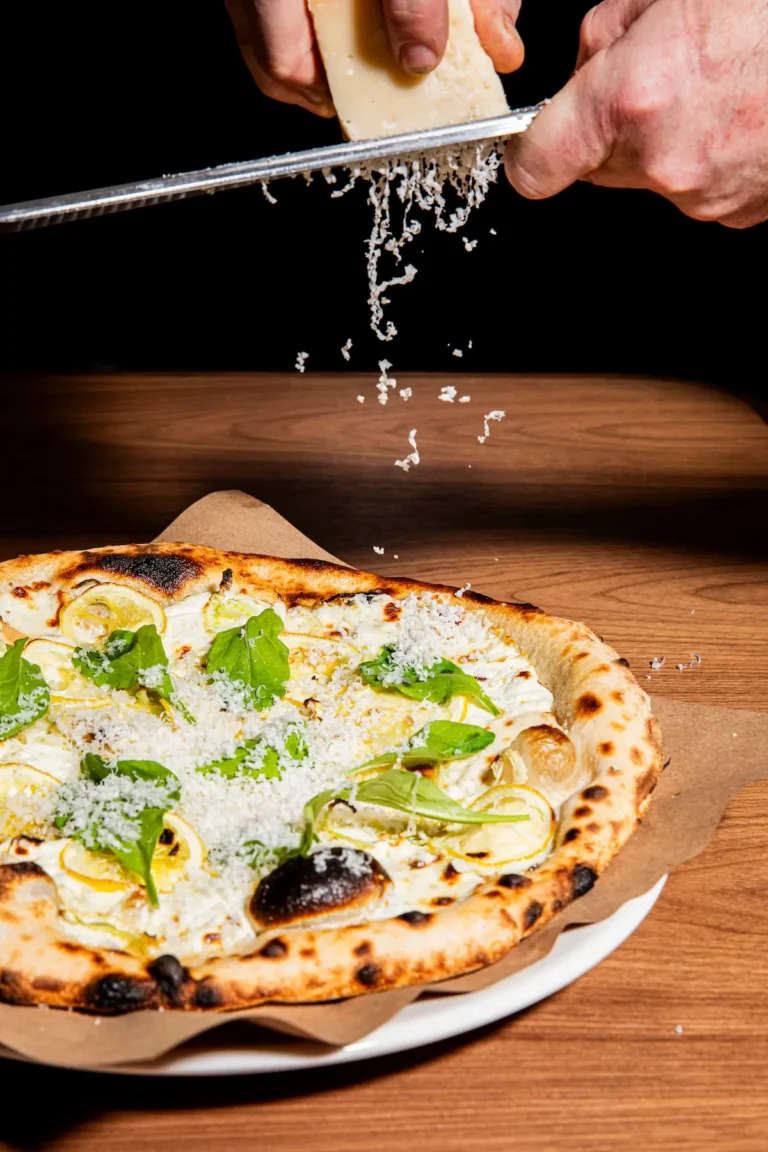 A chef grates cheese onto a lemon pizza