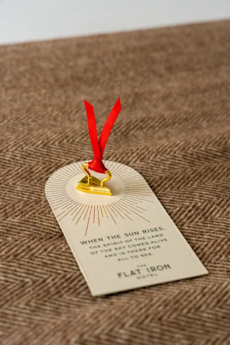 A golden iron token with a red ribbon sits atop the bedspread at the Flat Iron Hotel