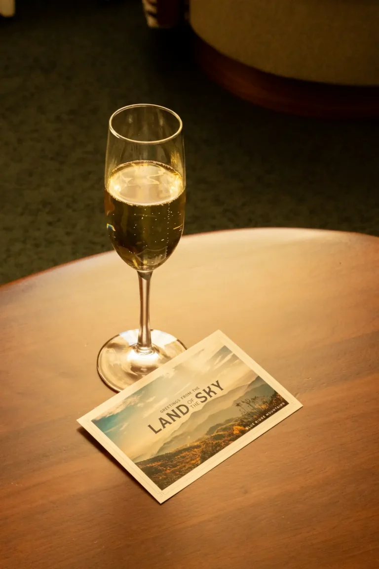 A glass of prosecco and a postcard sit on a table in the Premier King Suite at the Flat Iron Hotel