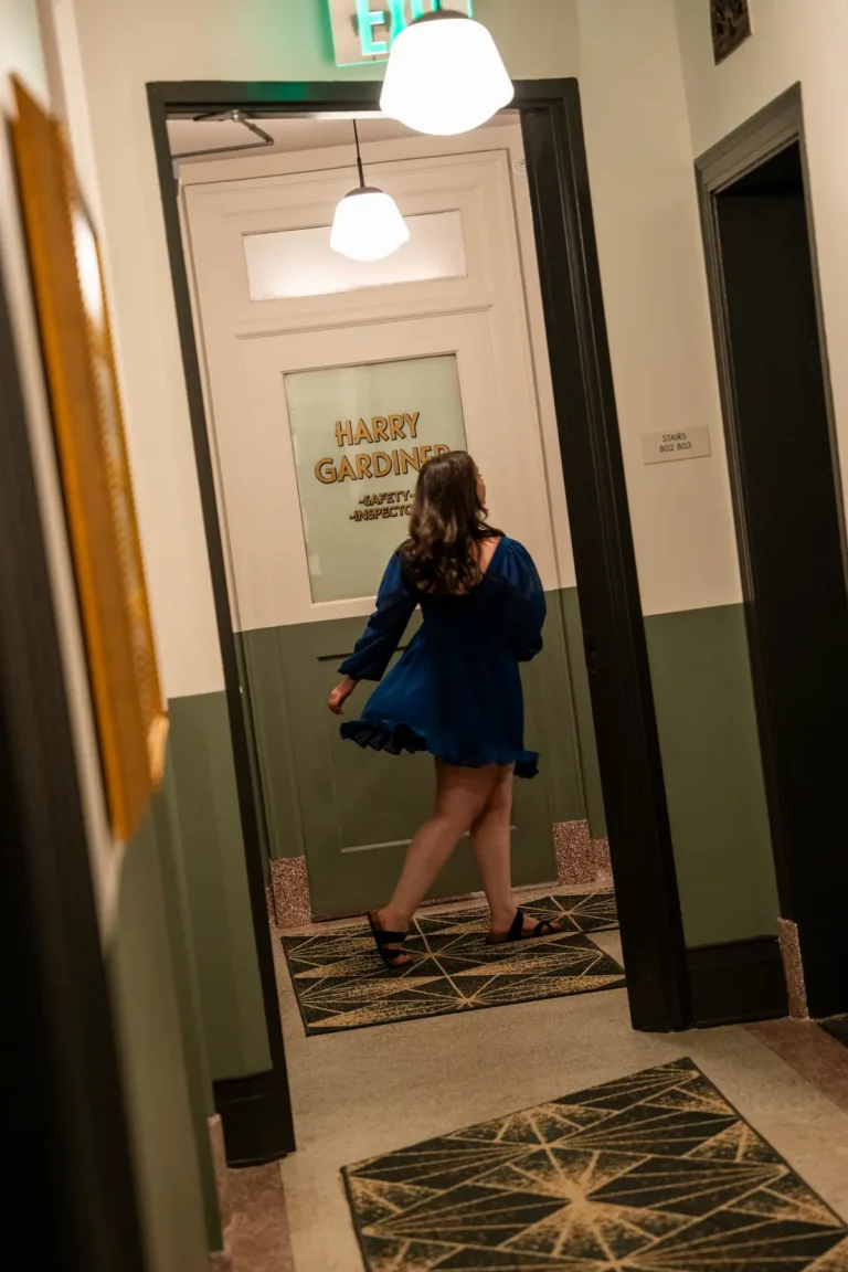 A woman in a dress strides through the guest corridor past vintage signage